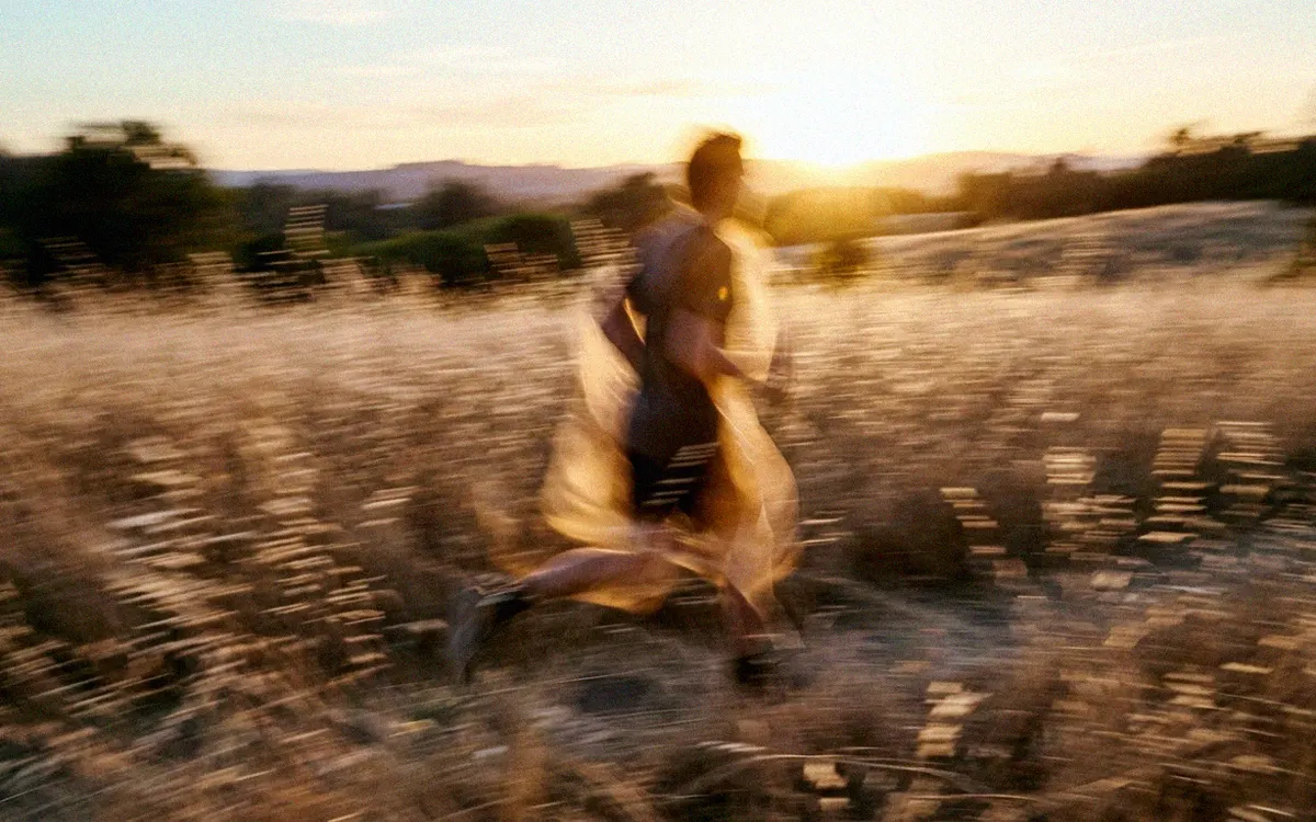 A person running through tall grass at golden hour, blurred by motion.