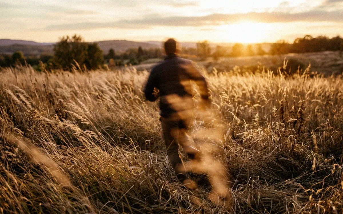 A person walking through tall grass at golden hour, blurred by motion.